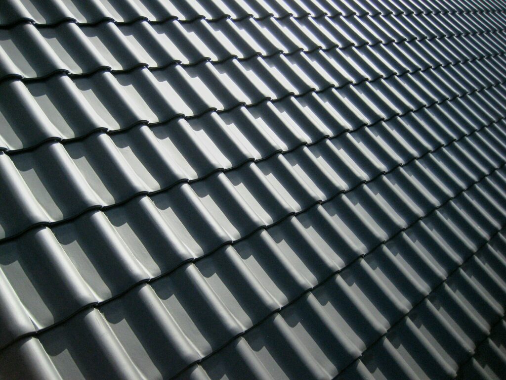A pattern of dark grey roof tiles with sharp shadows in bright light